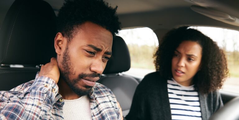Image of a man in the passenger seat of a car holding his neck in pain