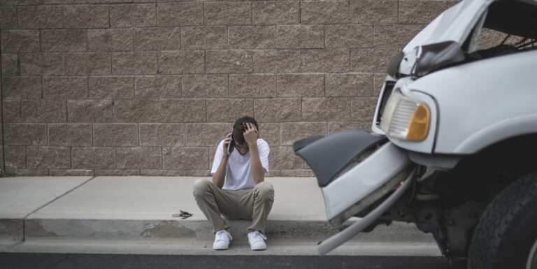 Image of a man sitting on the curb making a call after a car wreck