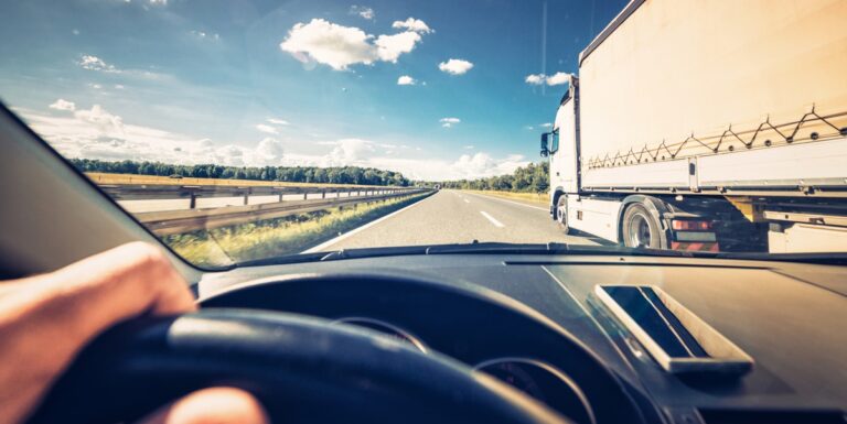 Image of the view out the windshield of a car, with a semi-truck in the adjacent lane