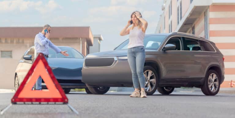 Image of a woman on the phone looking distressed and standing by two collided cars