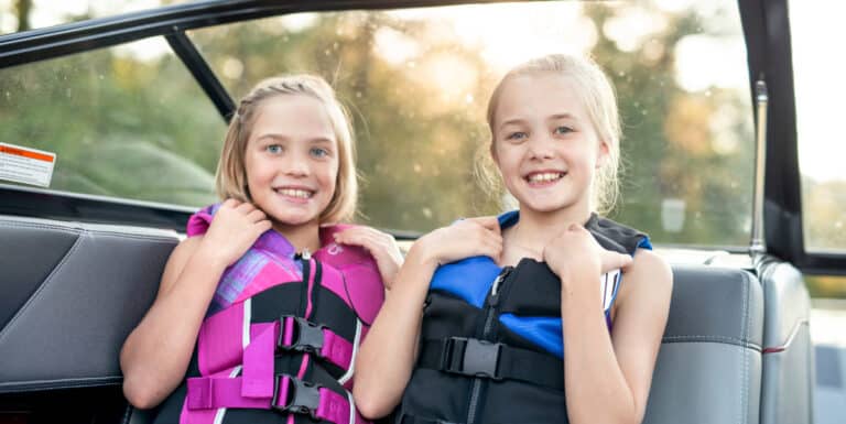 Image of two young girls on a boat smiling and wearing life jackets
