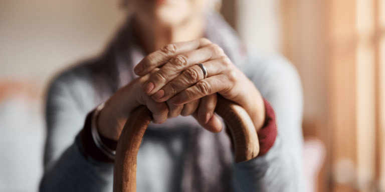 Image of a senior citizen sitting with her hands resting on a cane